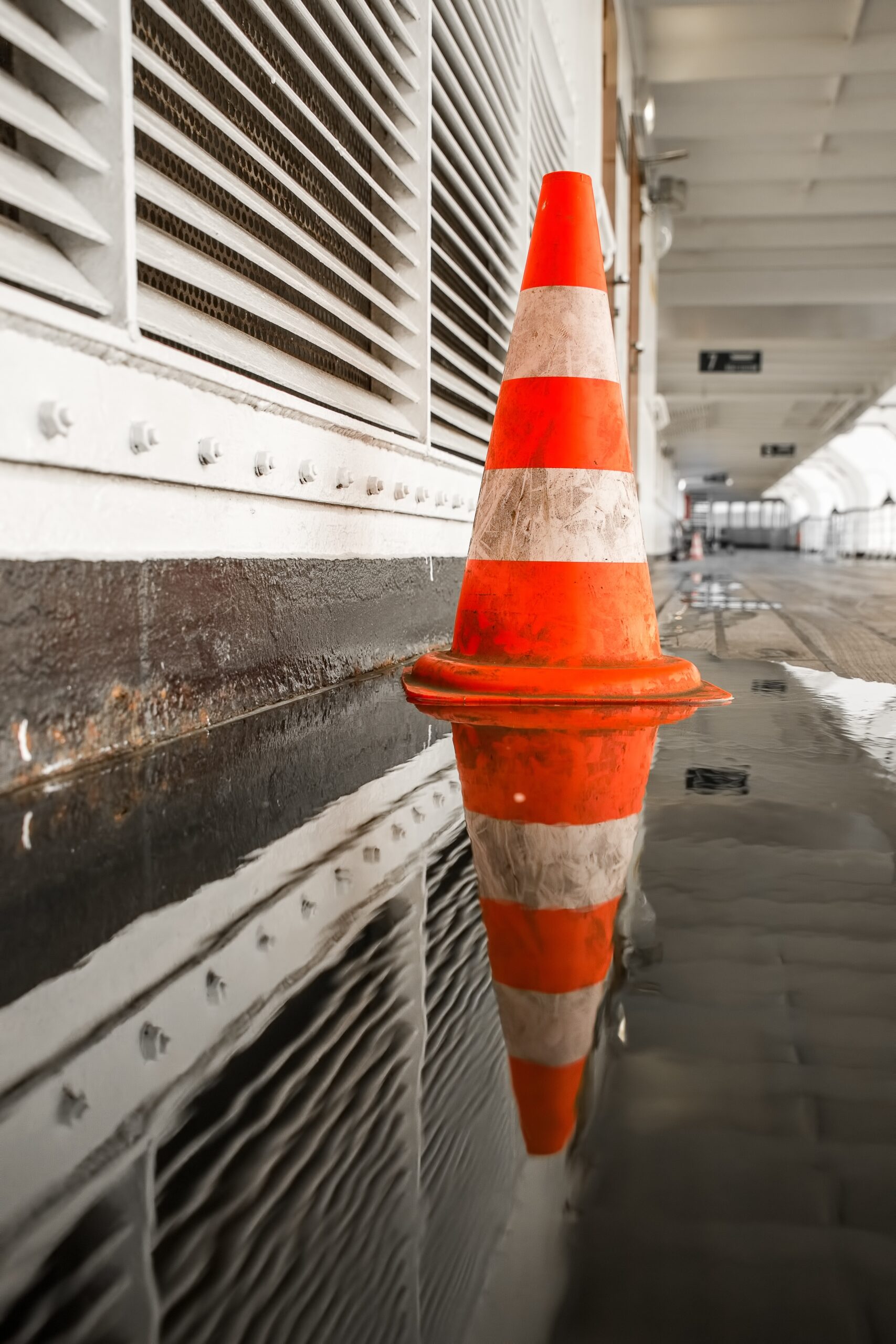 A selective shot of an orange traffic cone on the side of the hallway with a puddle reflecting it